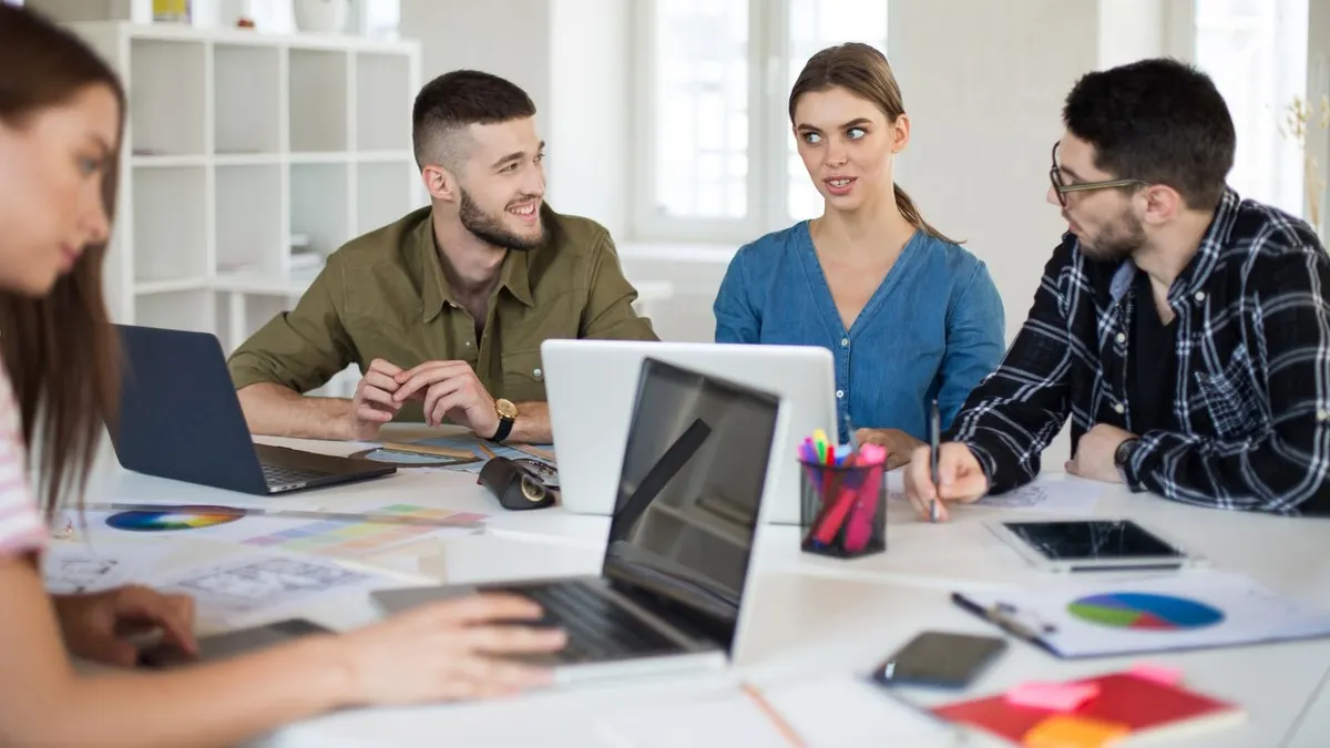 A small product team discussing a new project around a table of laptops and notes in a bright white office