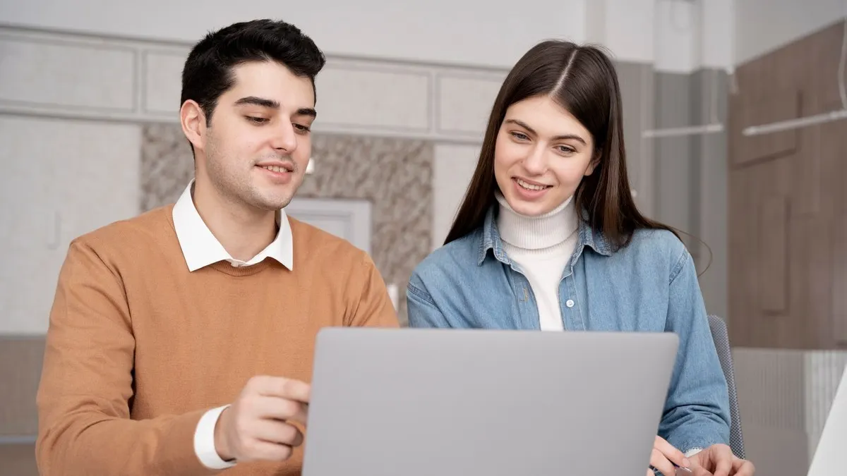 Two young colleagues smiling as they look at a laptop together in a bright office
