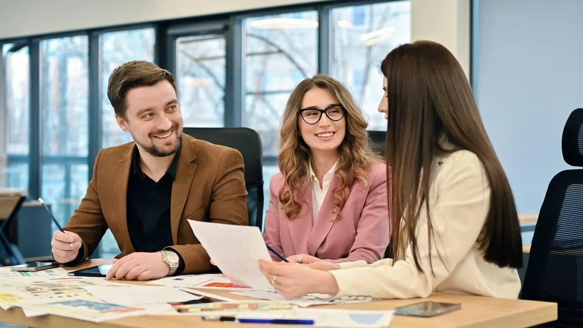 A smiling project team reviewing printed plans together at a meeting table in front of bright office windows