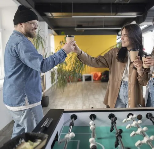 Two colleagues clinking coffee cups over a foosball table