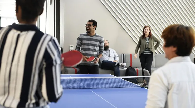 Colleagues playing table tennis in the office lounge