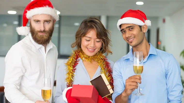 Three colleagues in Santa hats opening a gift at an office Christmas party