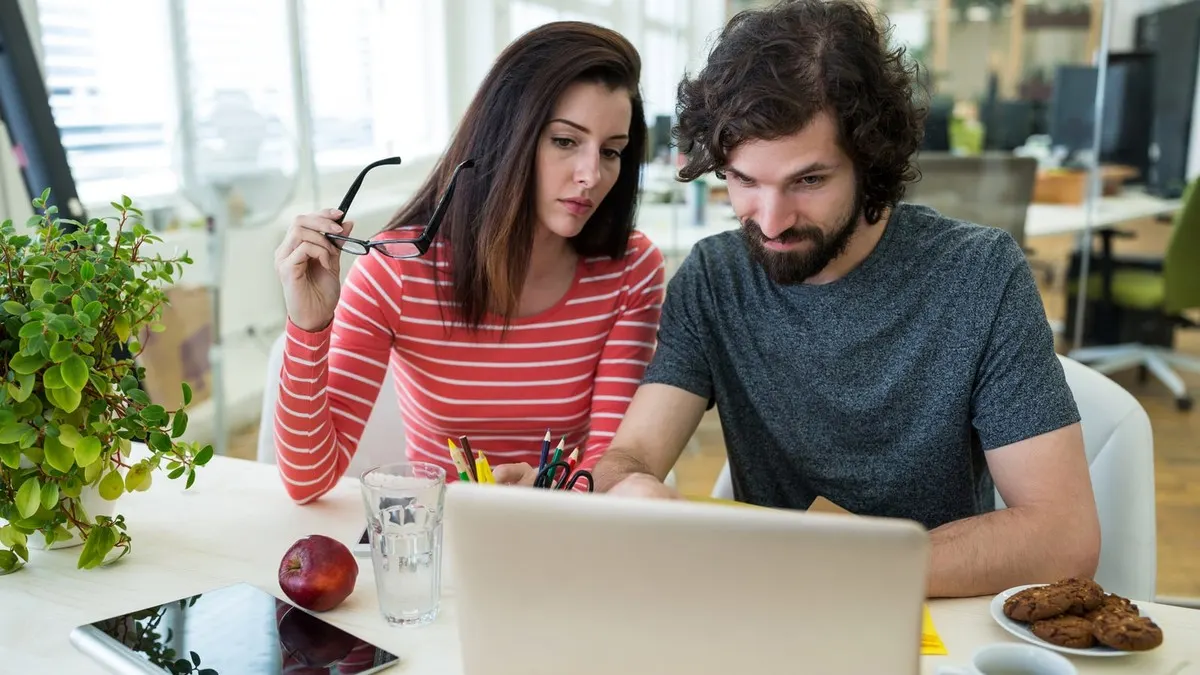 A man and a woman looking closely at a laptop screen together in a bright office