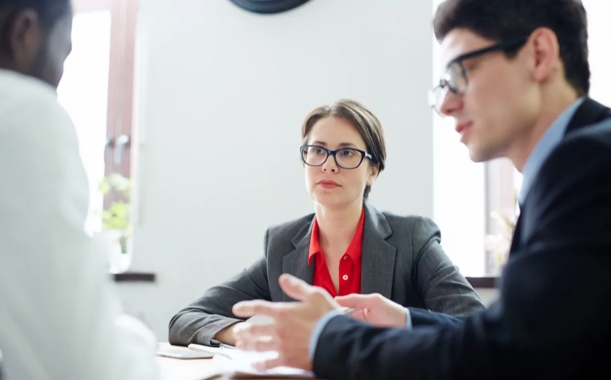 A woman in glasses listens closely across a desk