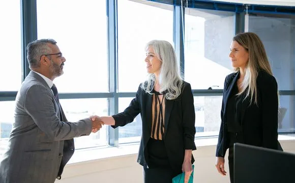 Two professionals shaking hands while a colleague looks on
